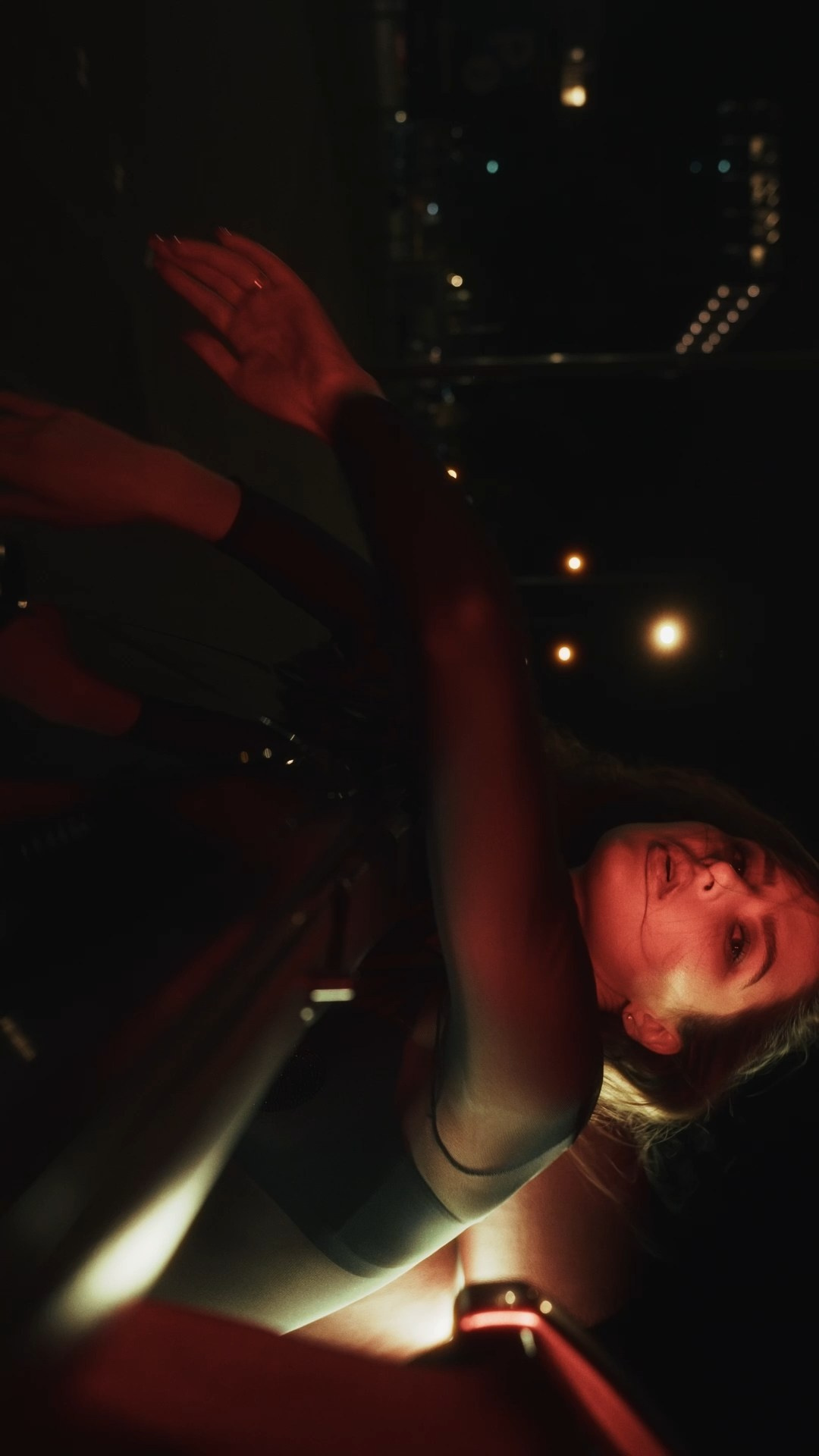 A tilted composition showing a person leaning back with their arms extended, captured in soft red light amidst a cityscape at night.