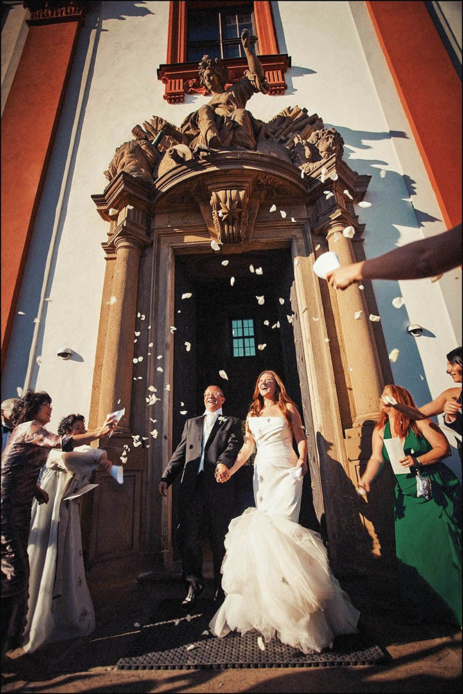 Newlyweds exiting Troja Chateau under rose petals and rice