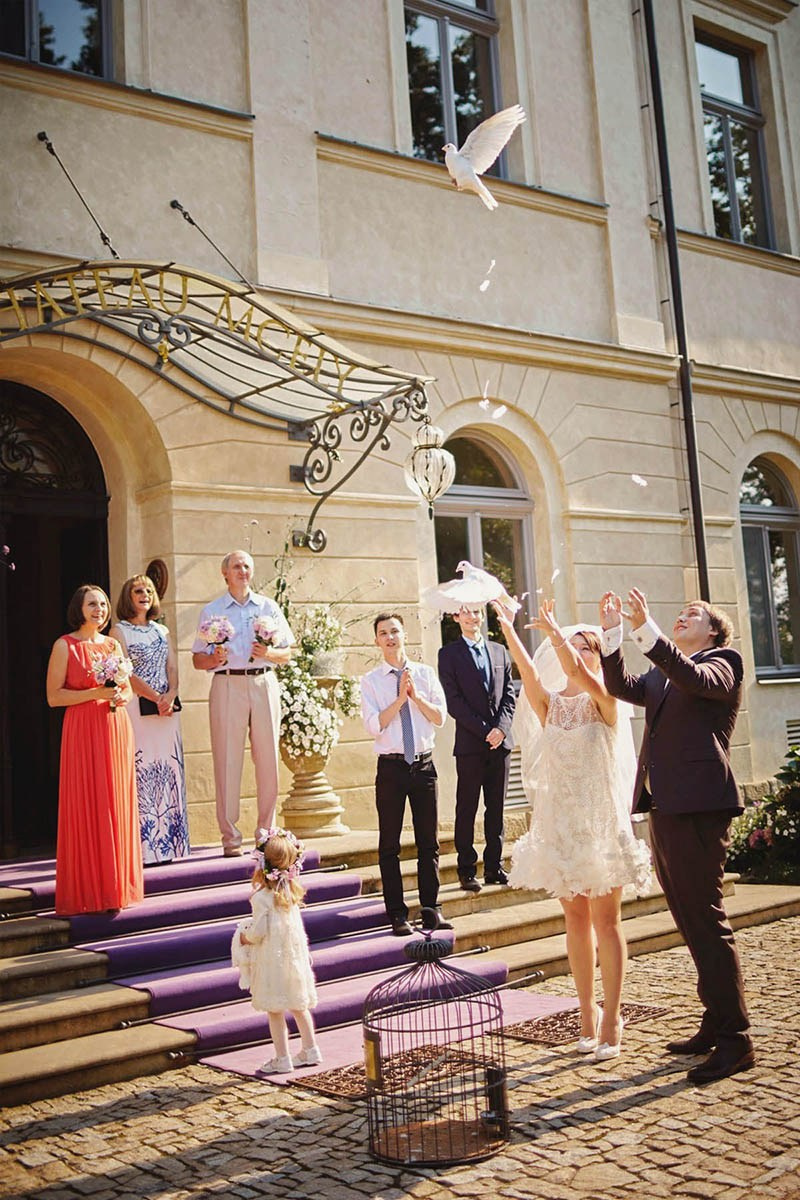A couple release white doves as wedding guests look on on the steps of Chateau Mcely