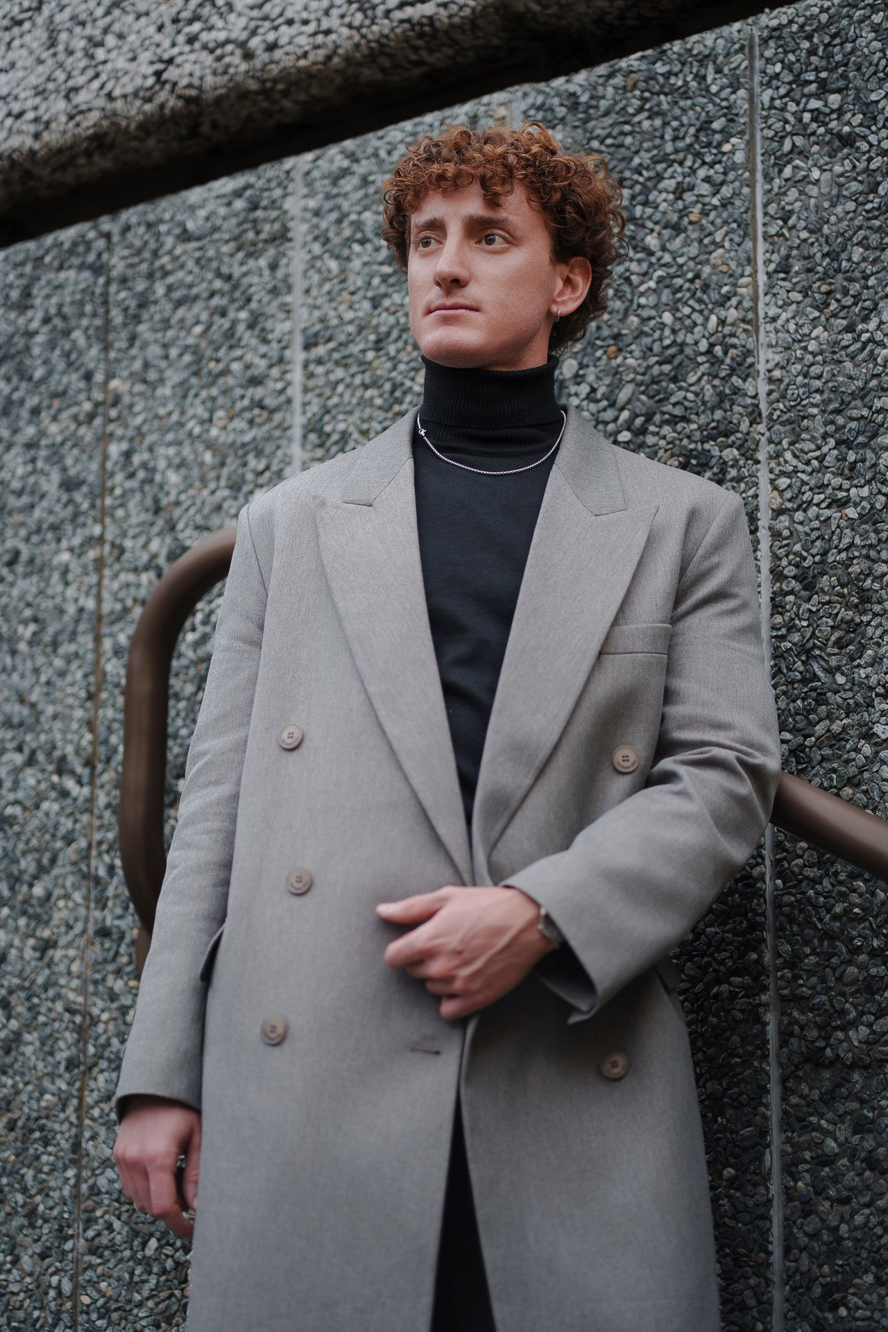 Man in grey double breasted coat posing against wall at Pitti Uomo 109