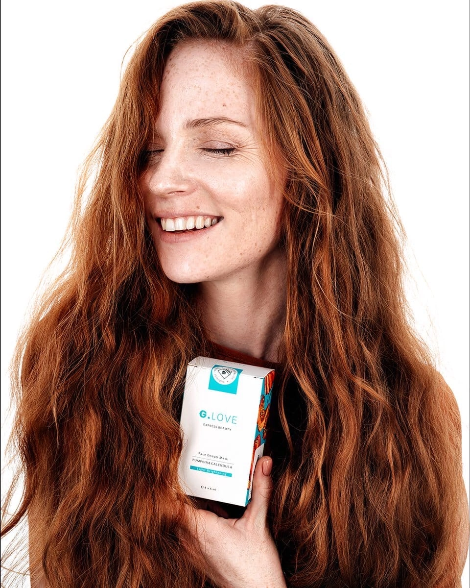 Redhead model with her eyes closed, creating a peaceful and introspective mood. Her hair cascades around her shoulders, and her makeup is flawless, highlighting her natural features. The lighting is soft, adding to the ethereal quality of the photograph, which emphasizes tranquility and inner beauty.