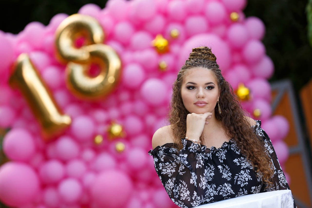 Stilizovana fotografija devojke sa zlatnim balonima na proslavi punoletstva. Portret slavljenice na tematskoj dekoraciji za 18. rođendan.