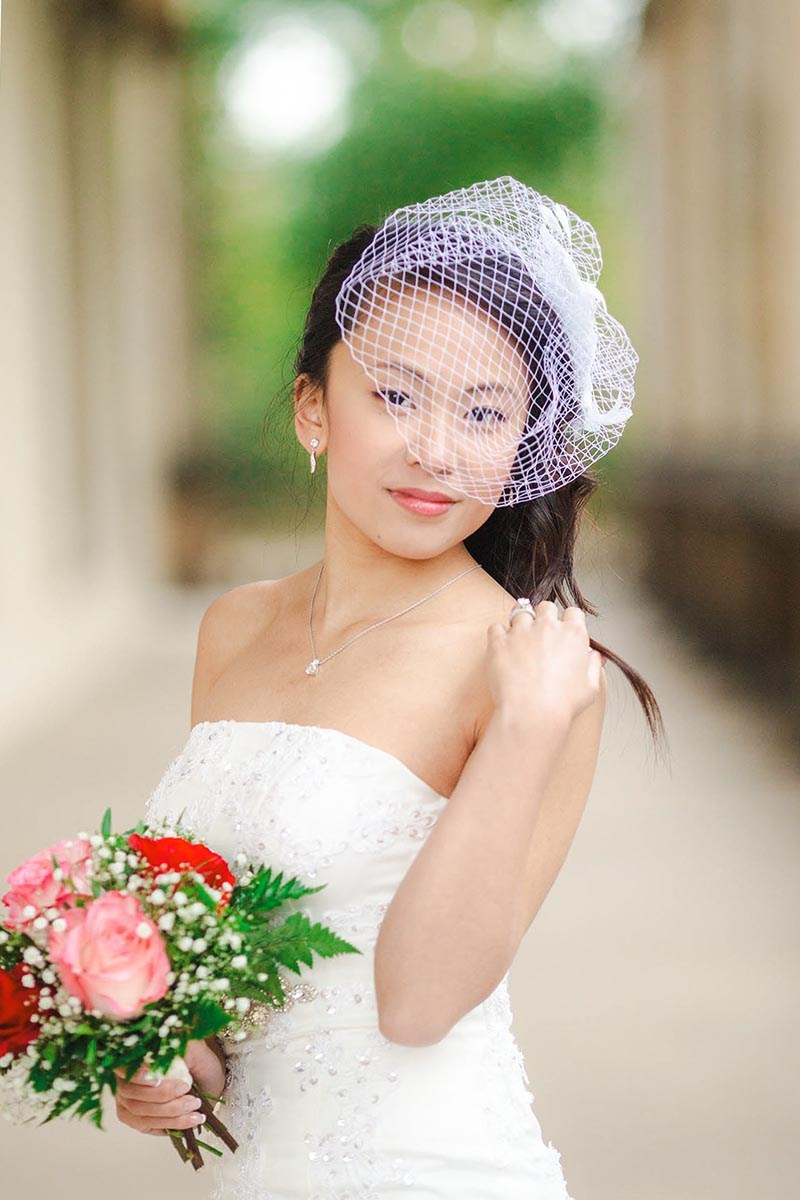 Asian bride with bird-cage veil playing with her hair during her portrait session at Prague Castle.