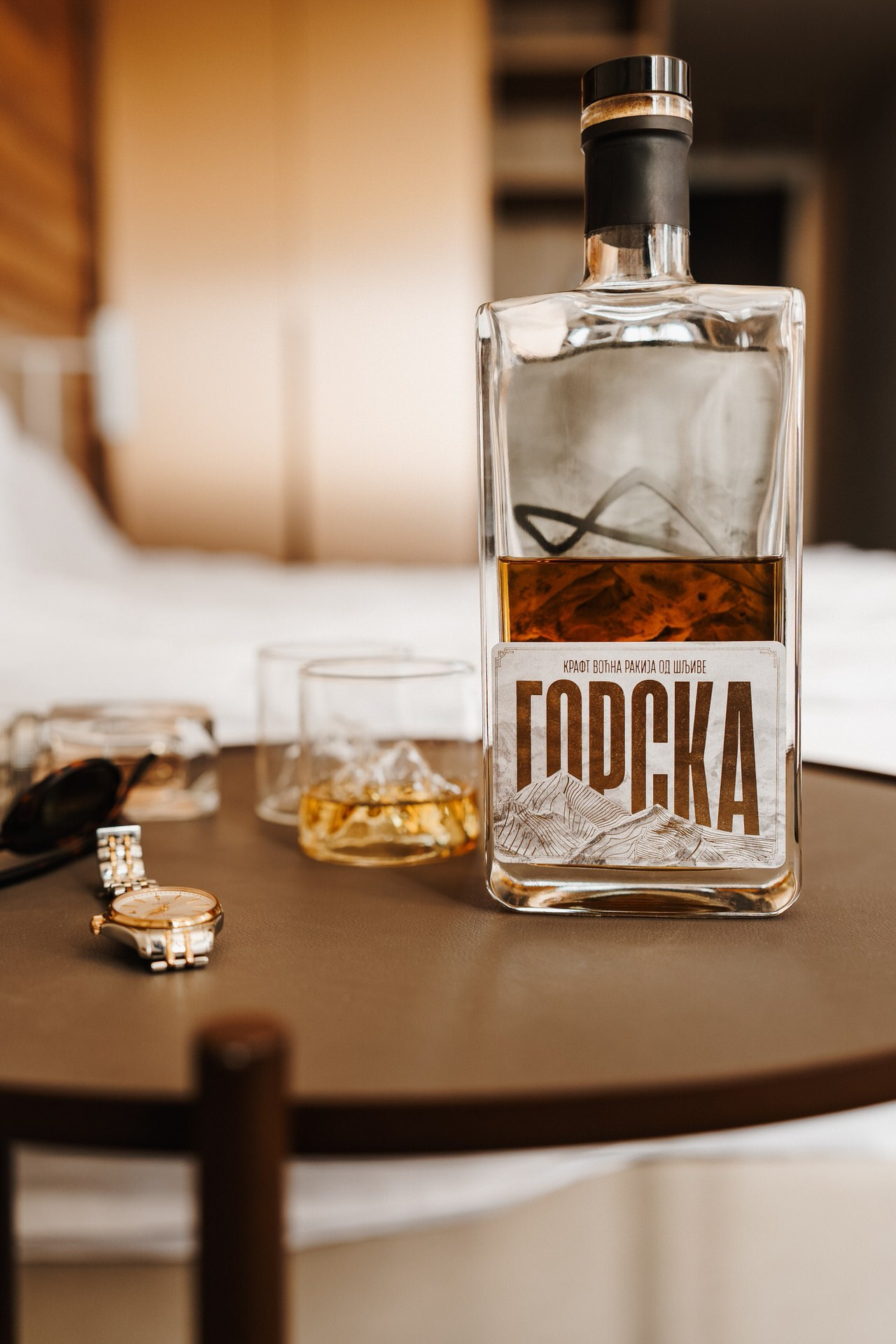 rakija Gorska na stoliću sa čašom i satom u pozadini