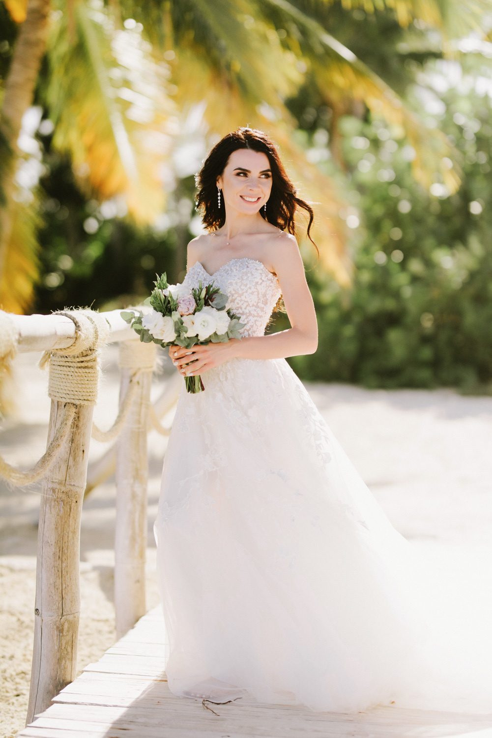 Невеста на мостике у деревянных перил на фоне пальмы.