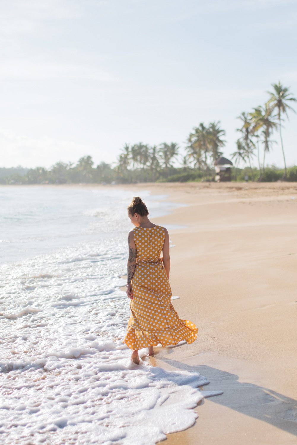 The bride walks on the sea water at the very edge of the beach with palm trees.