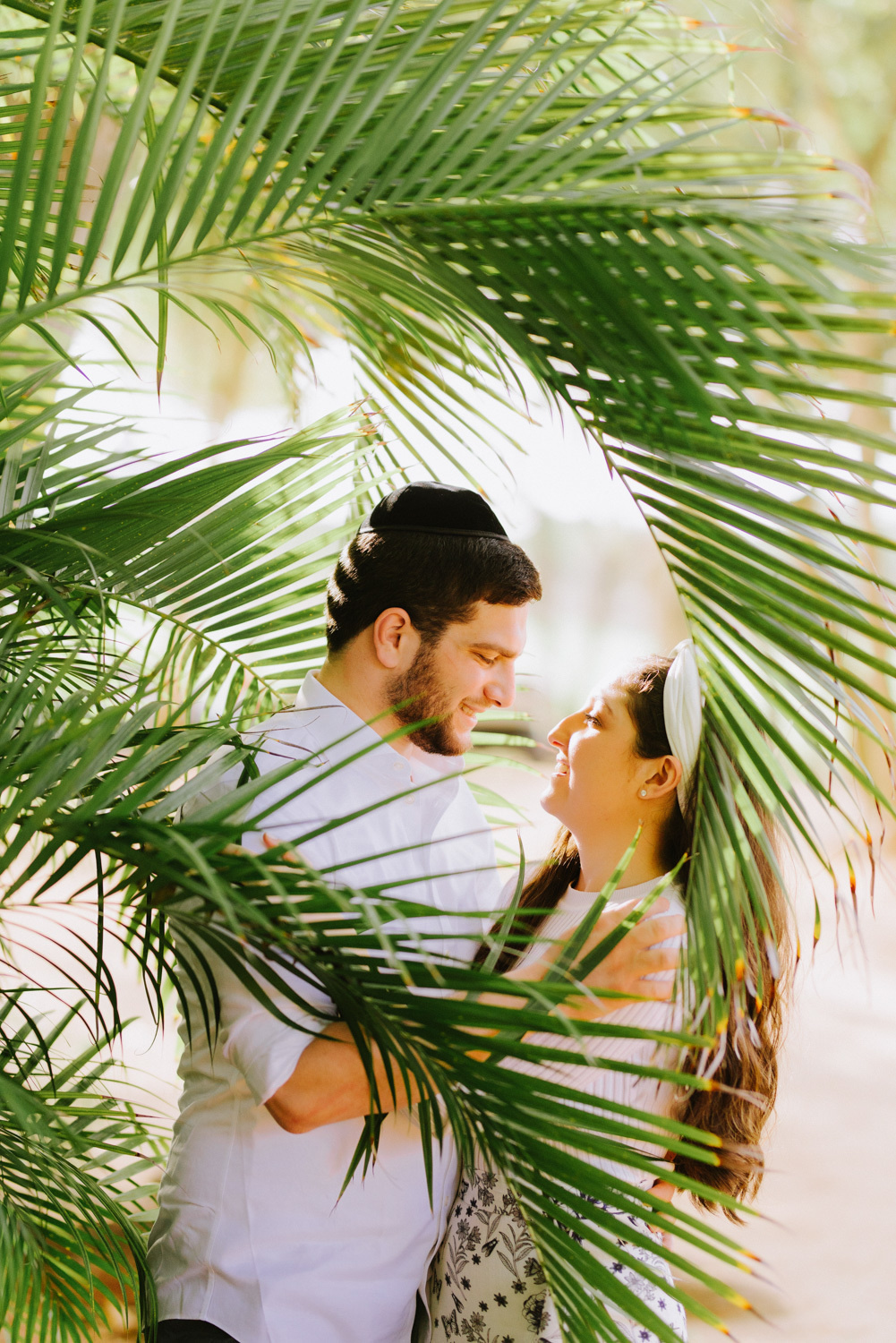 Bride and groom look at each other in the shade of a palm tree.