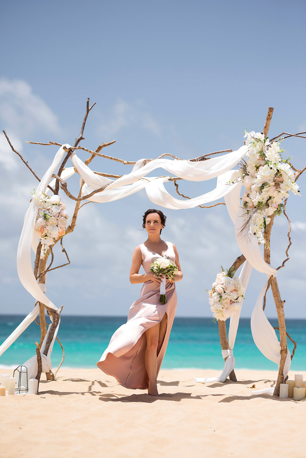 Невеста с букетом цветов под свадебным алтарем на фоне бирюзового океана и голубого неба.