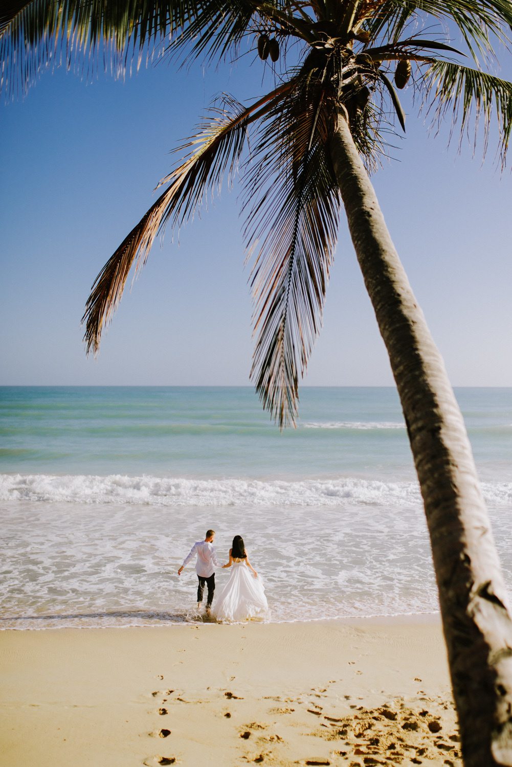From a huge palm tree, the bride and groom go to the sea, leaving their footprints in the sand.