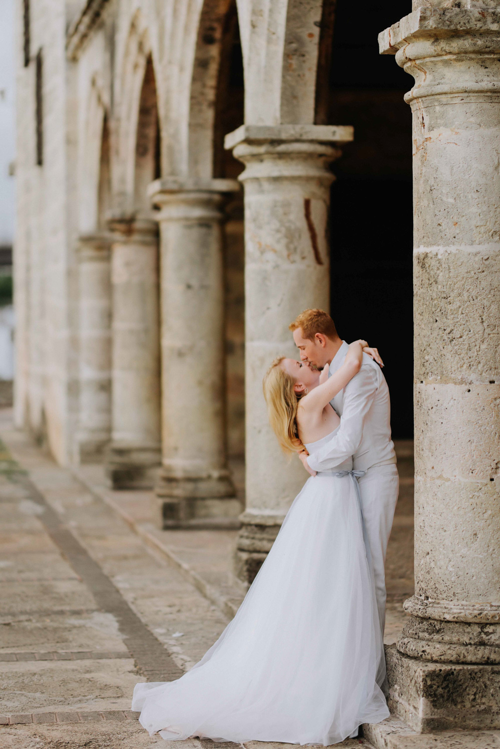 Жених целует невесту на фоне колонн здания.