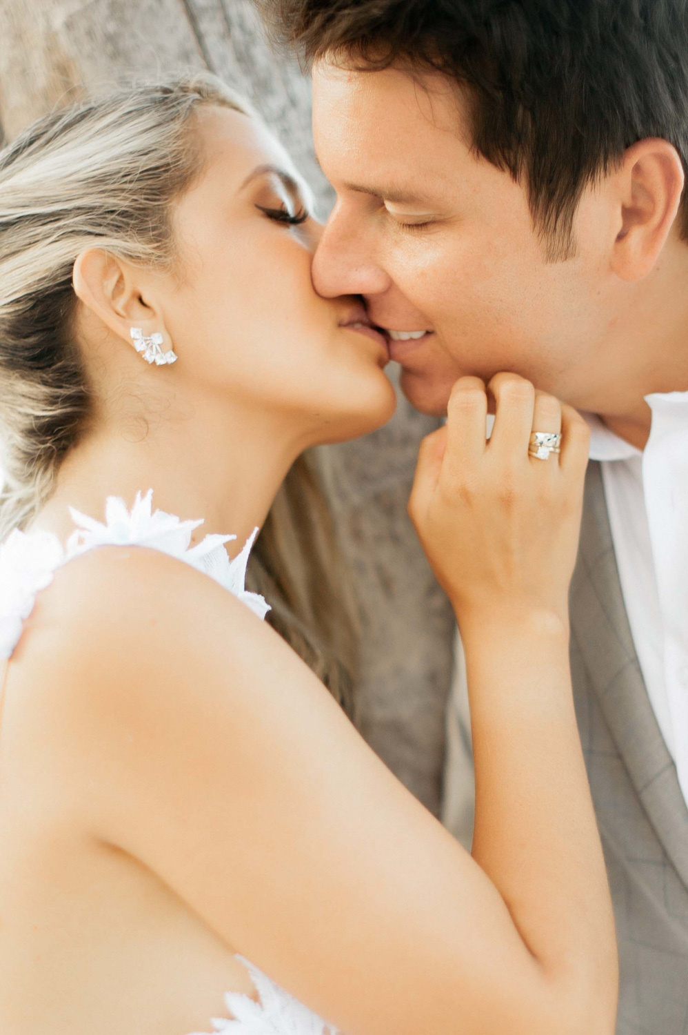 Faces of newlyweds kissing. The bride has white earrings and a ringlet.