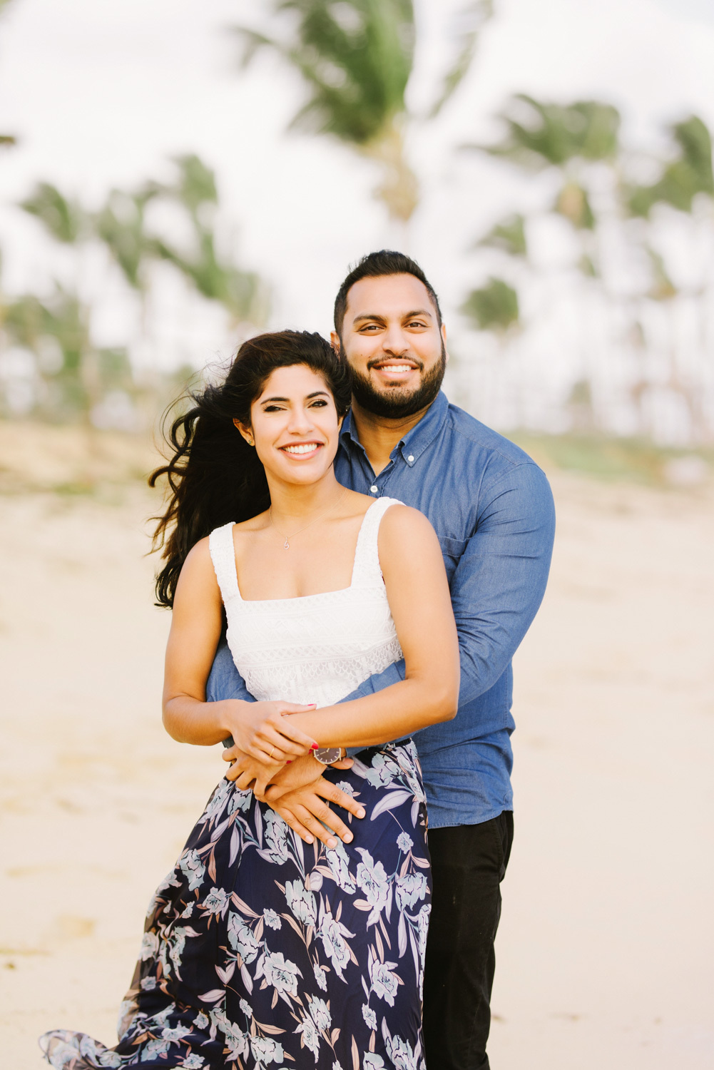 Жених сзади обнимает невесту на размытом фоне пальм.