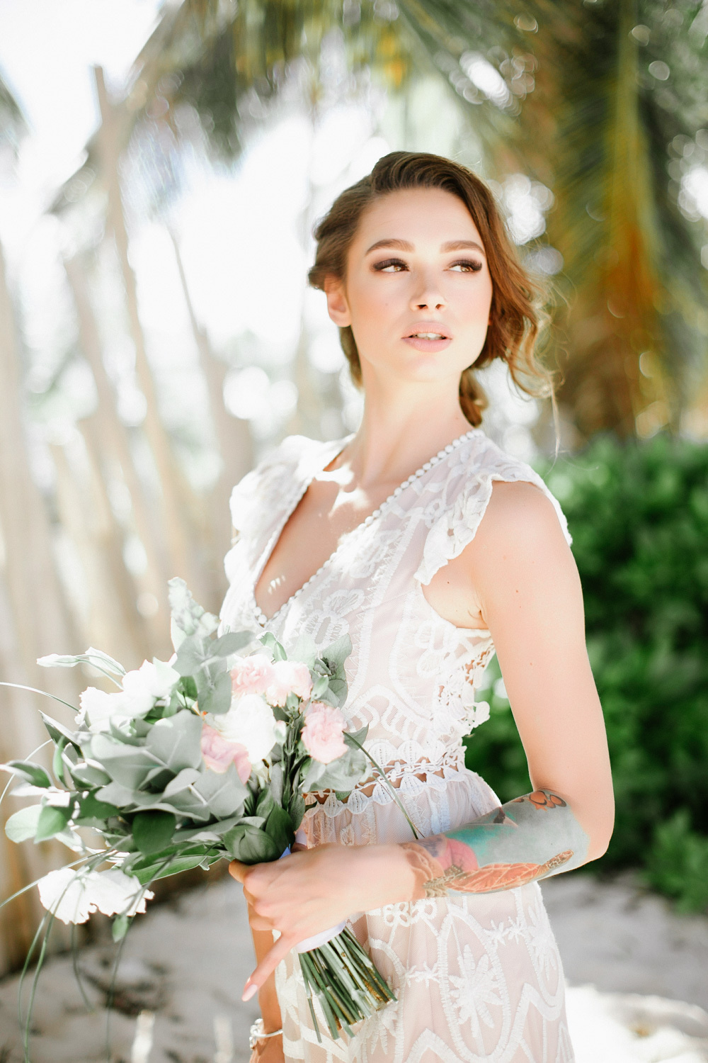 Bride with a bouquet of flowers on the background of palm trees in the sunlight.