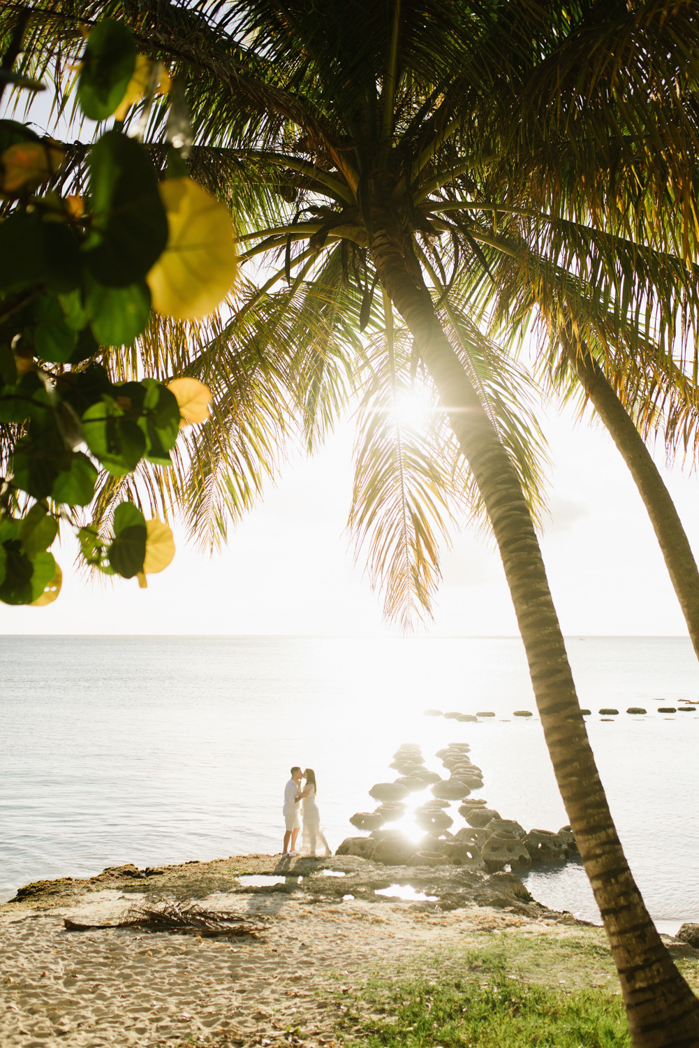 Silhouettes of the bride and groom on the beach with palm trees on the background of the sea.