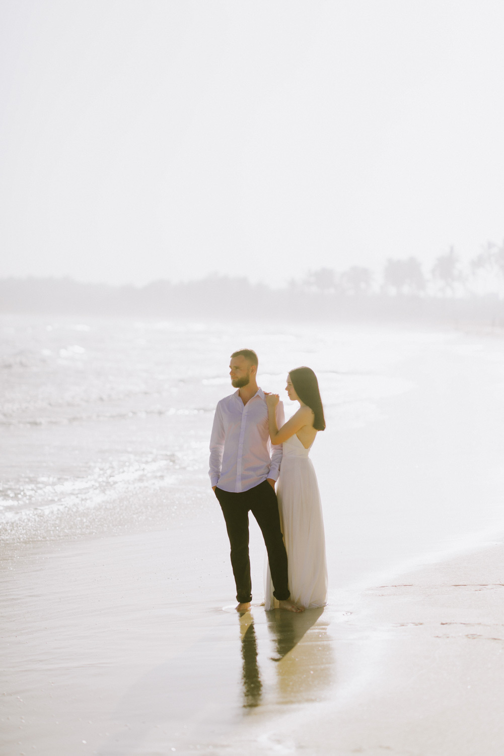 The bride and groom look out into the sunlit sea.