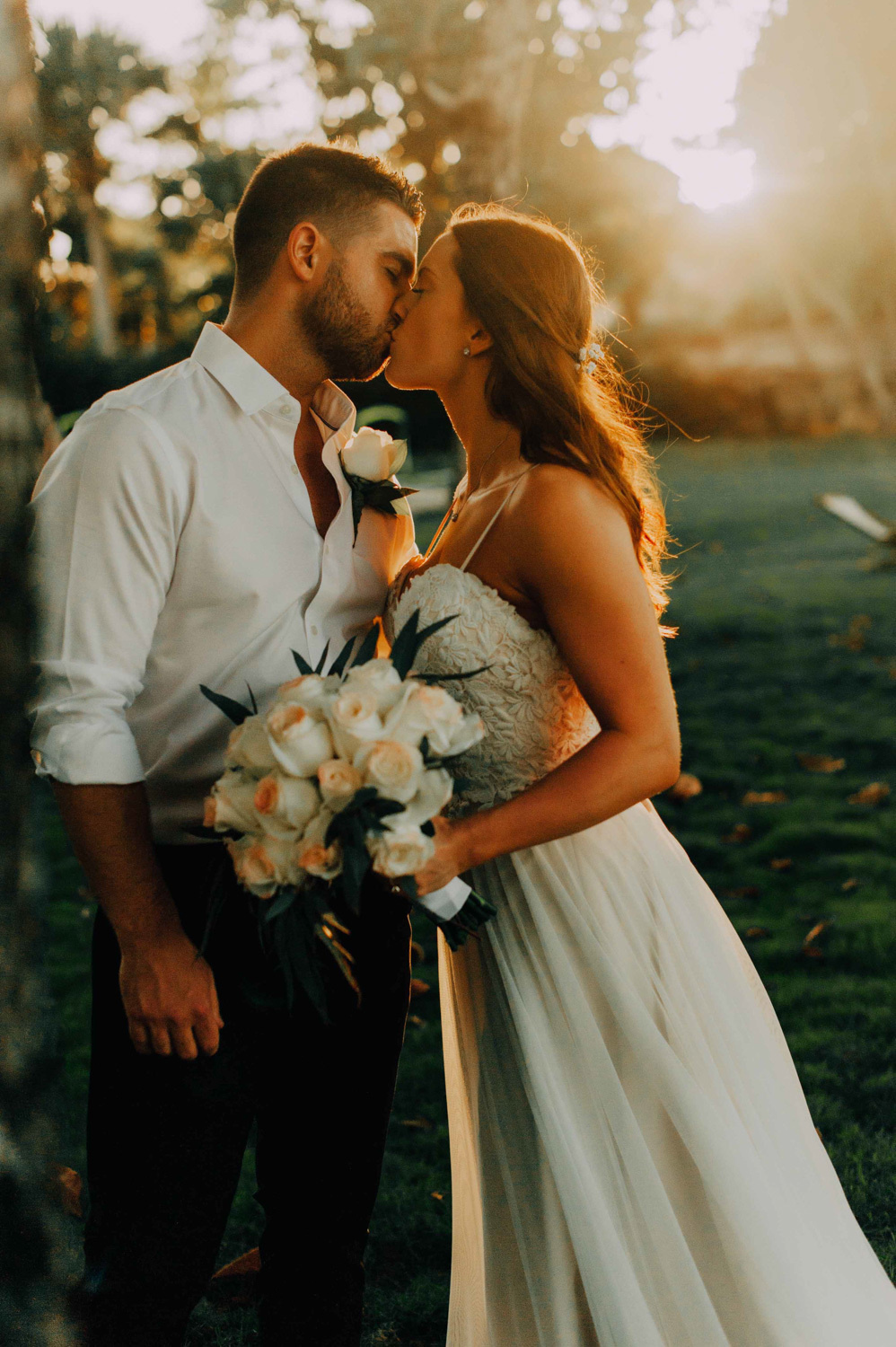 The bride and groom kiss each other in the setting sun.