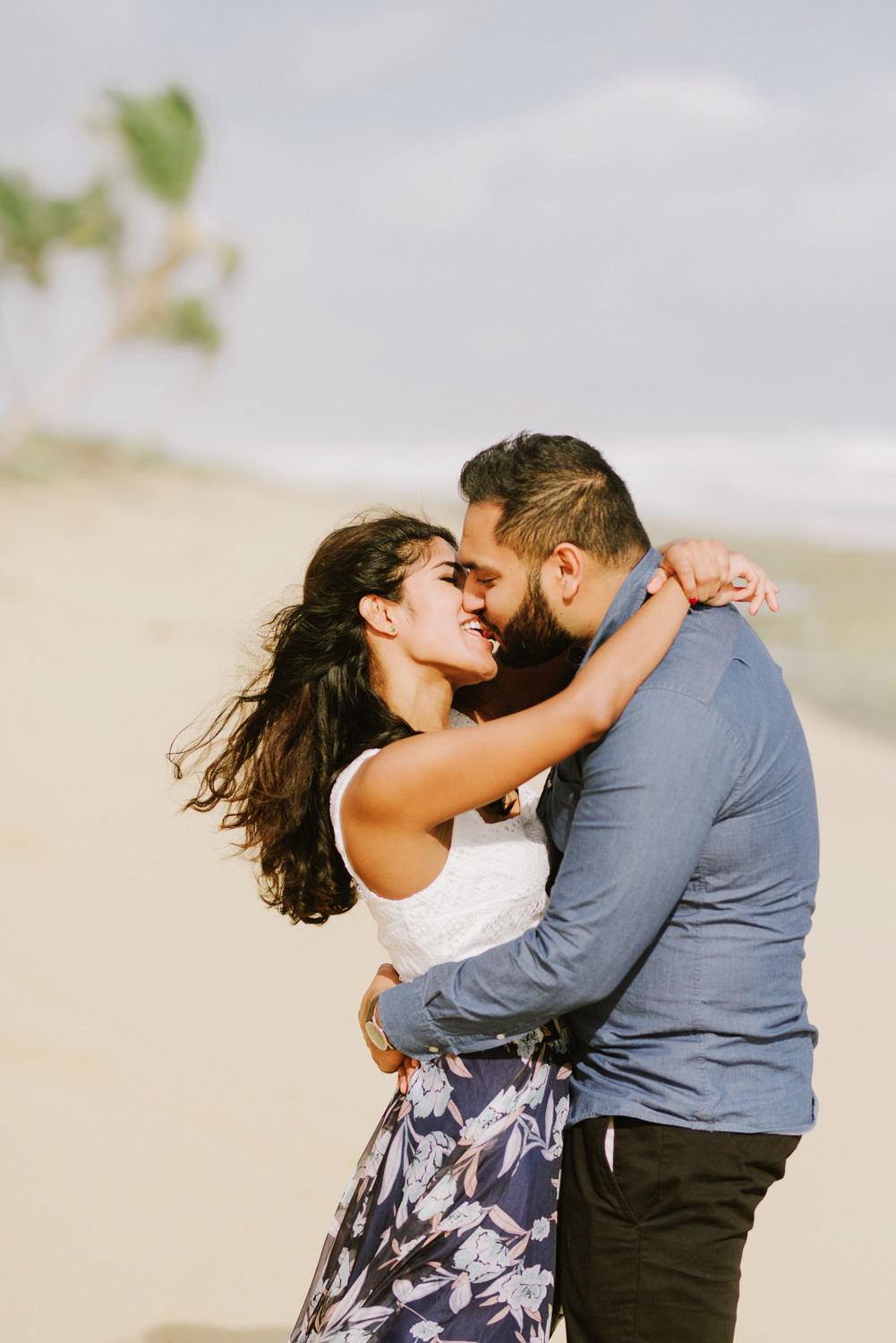 Жених с невестой целуются на фоне песчаного пляжа.