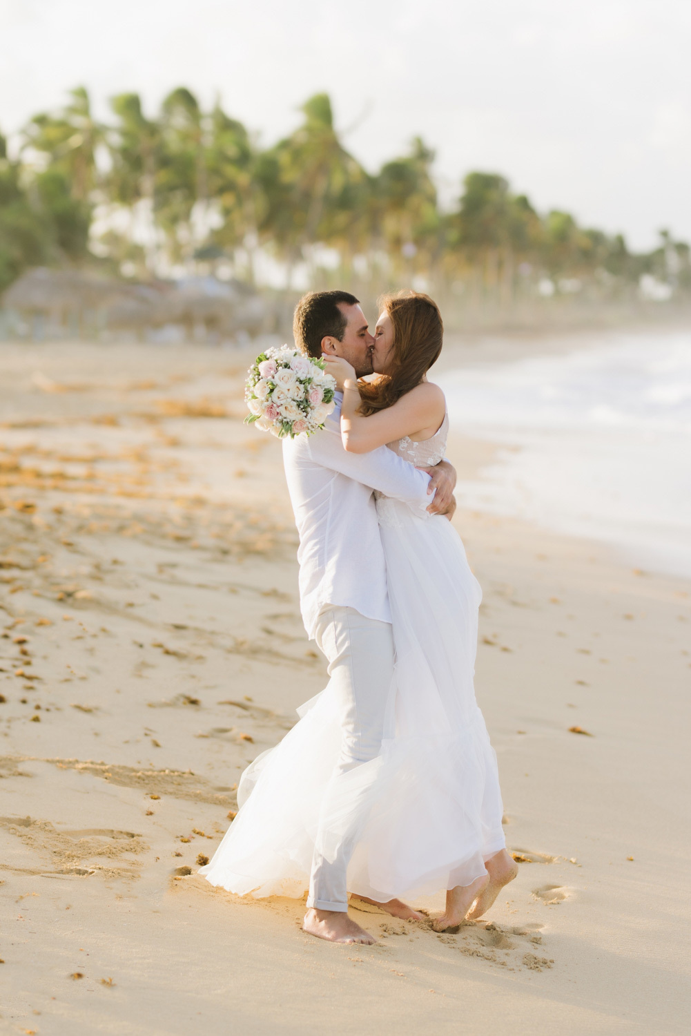 on a sandy beach, the groom pulled the bride to him and kissed her, the bride stood on tiptoes
