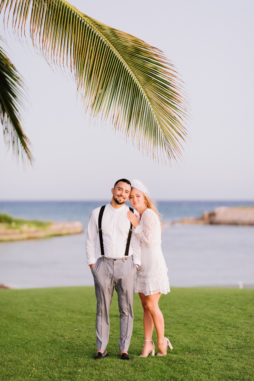 Bride and groom on a green lawn near a palm tree on the background of the sea bay.