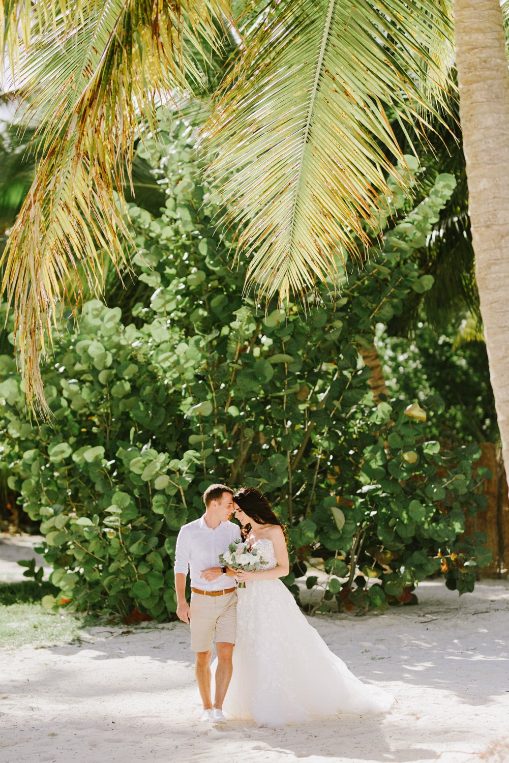 Невеста с женихом под пальмой на фоне зеленого куста.