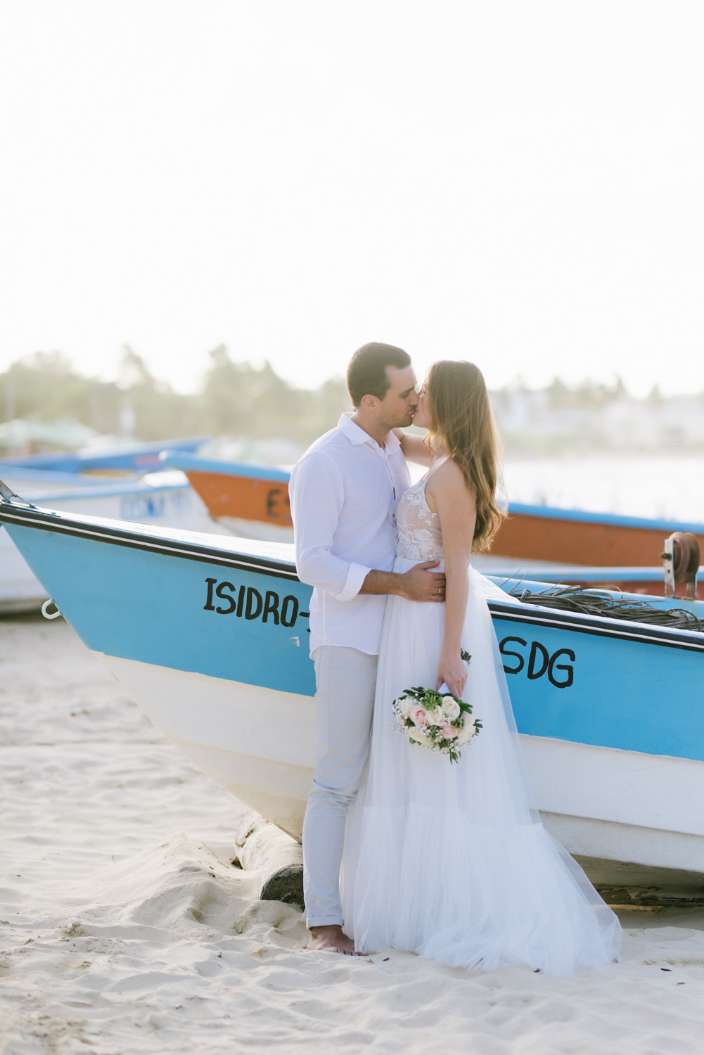 kissing wedding couple at a wooden boat on the beach, the bride in the hands of a wedding bouquet