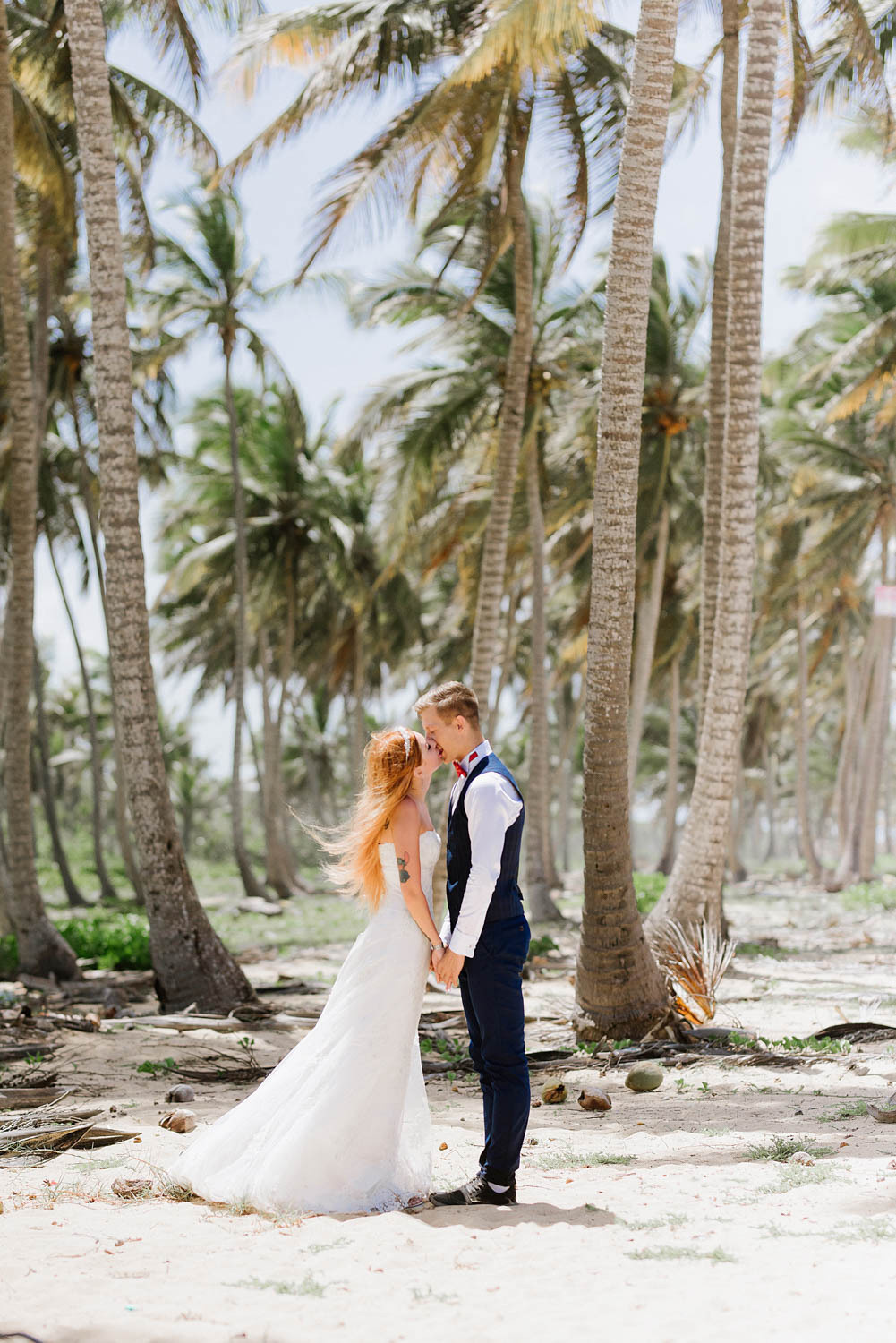 Among the many tall palm trees, the bride and groom look into each other's eyes, holding hands.