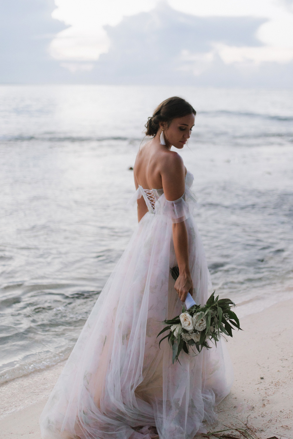 Невеста в прозрачном лёгком белом платье на фоне белых морских волн.