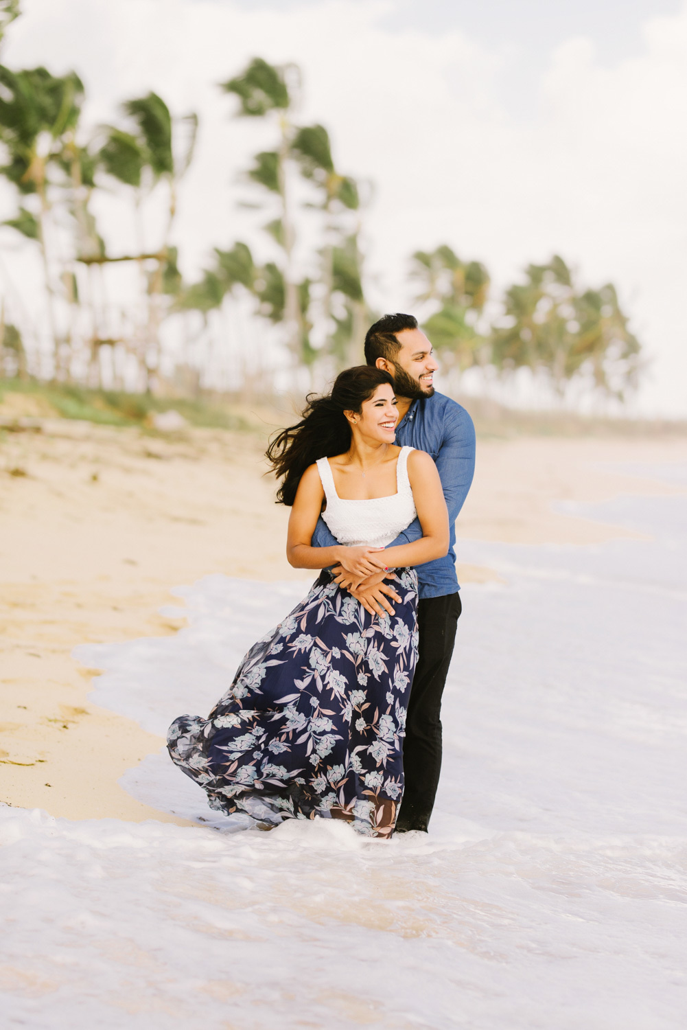 Жених с невестой смотрят в море на фоне песчаного берега с пальмами.