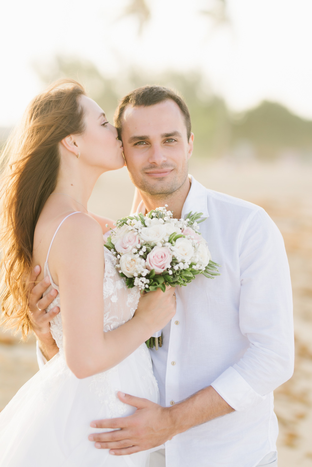 the bride with a wedding bouquet in her right hand hugs and kisses the groom on the temple, middle plan photo