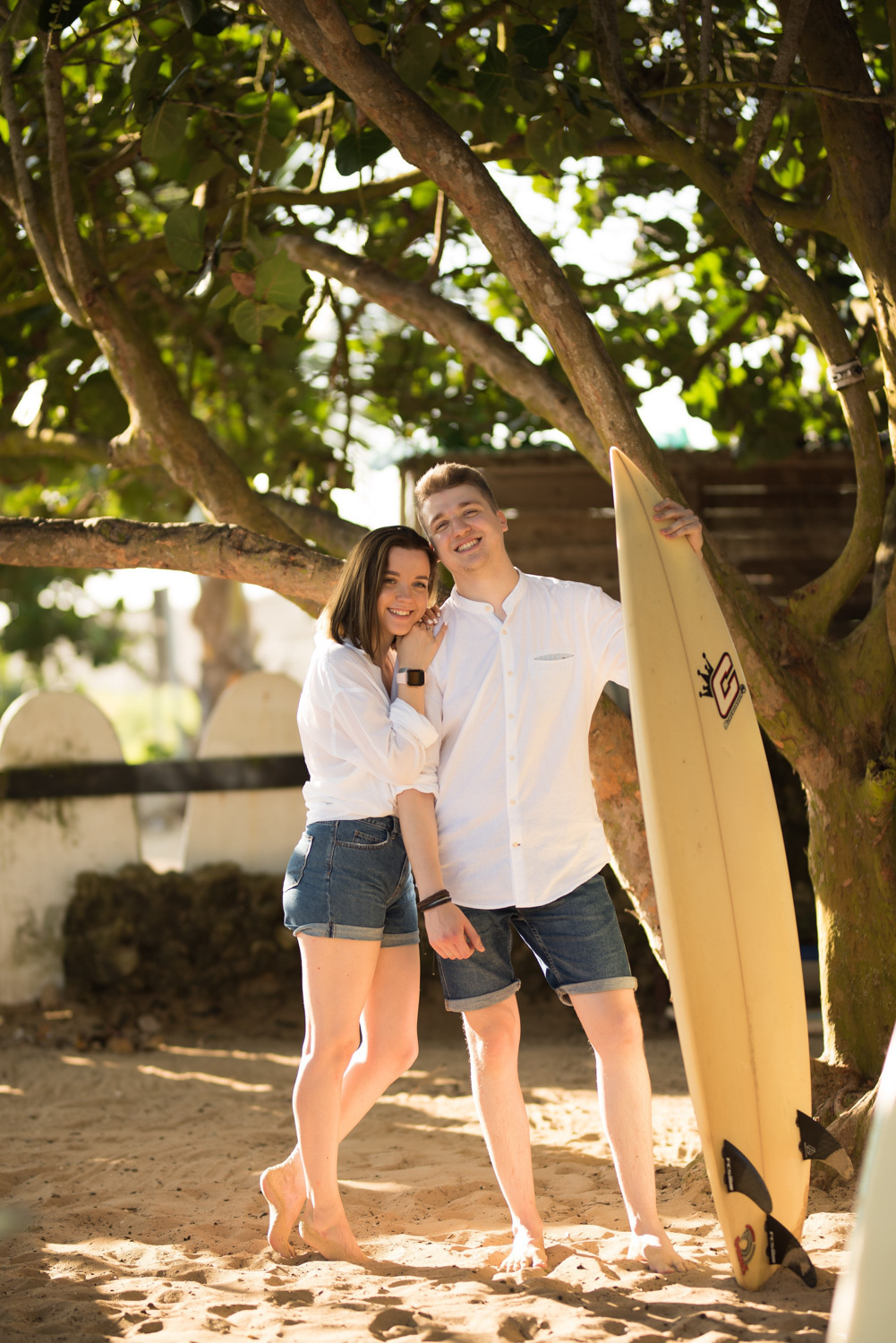 Bride and groom on a sandy beach under a tree.