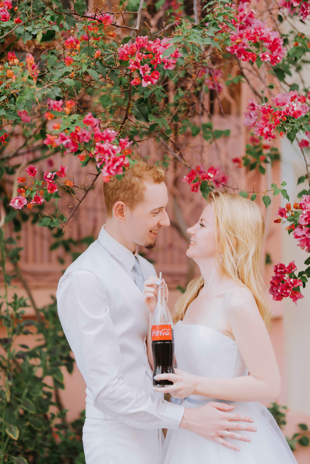 Жених с невестой обнимаются на фоне красных цветов.