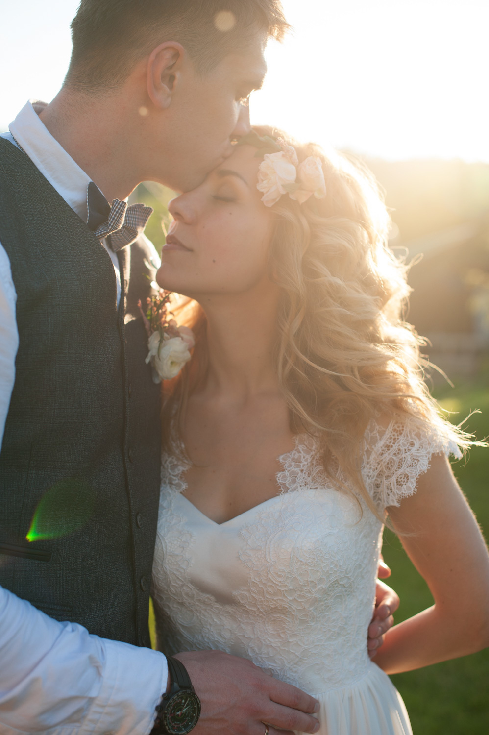 The groom kisses the bride on the forehead against the background of sunlight.