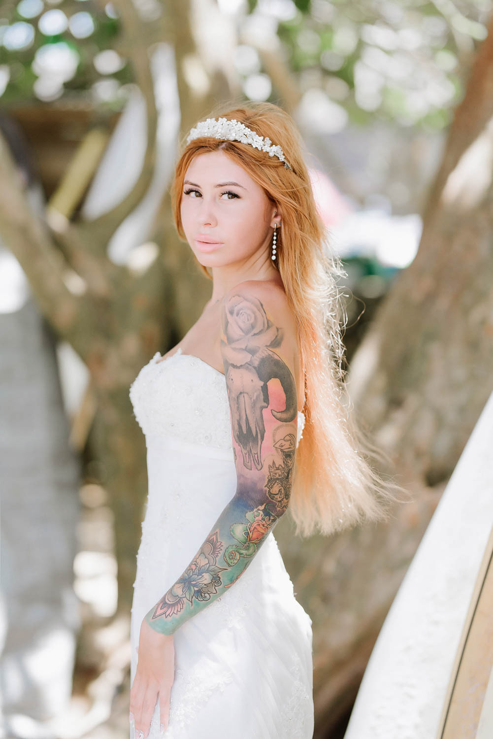 The bride, turned sideways, looks at the photographer against the background of tree trunks.