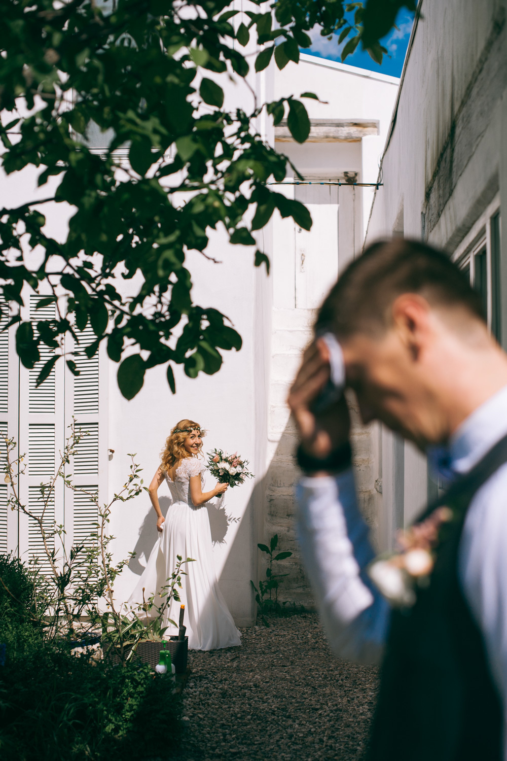 The bride looks at the groom, who has lowered his head, from the back of the courtyard.