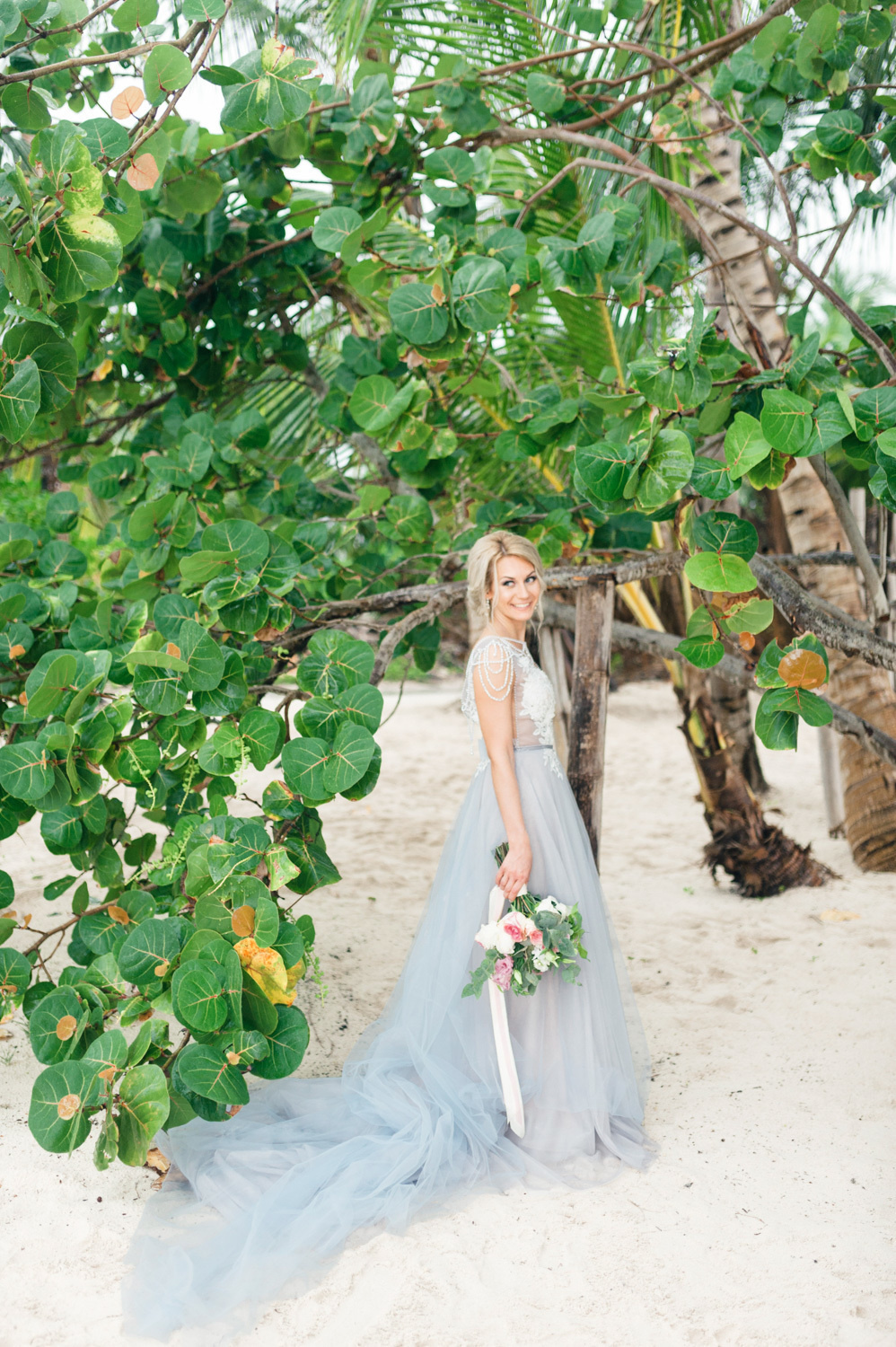 Bride with a bouquet of flowers on the beach under a tree.