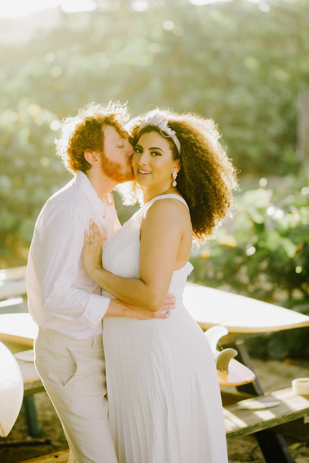 У деревянного столика с лавочками жених обнимает невесту на зеленом фоне.