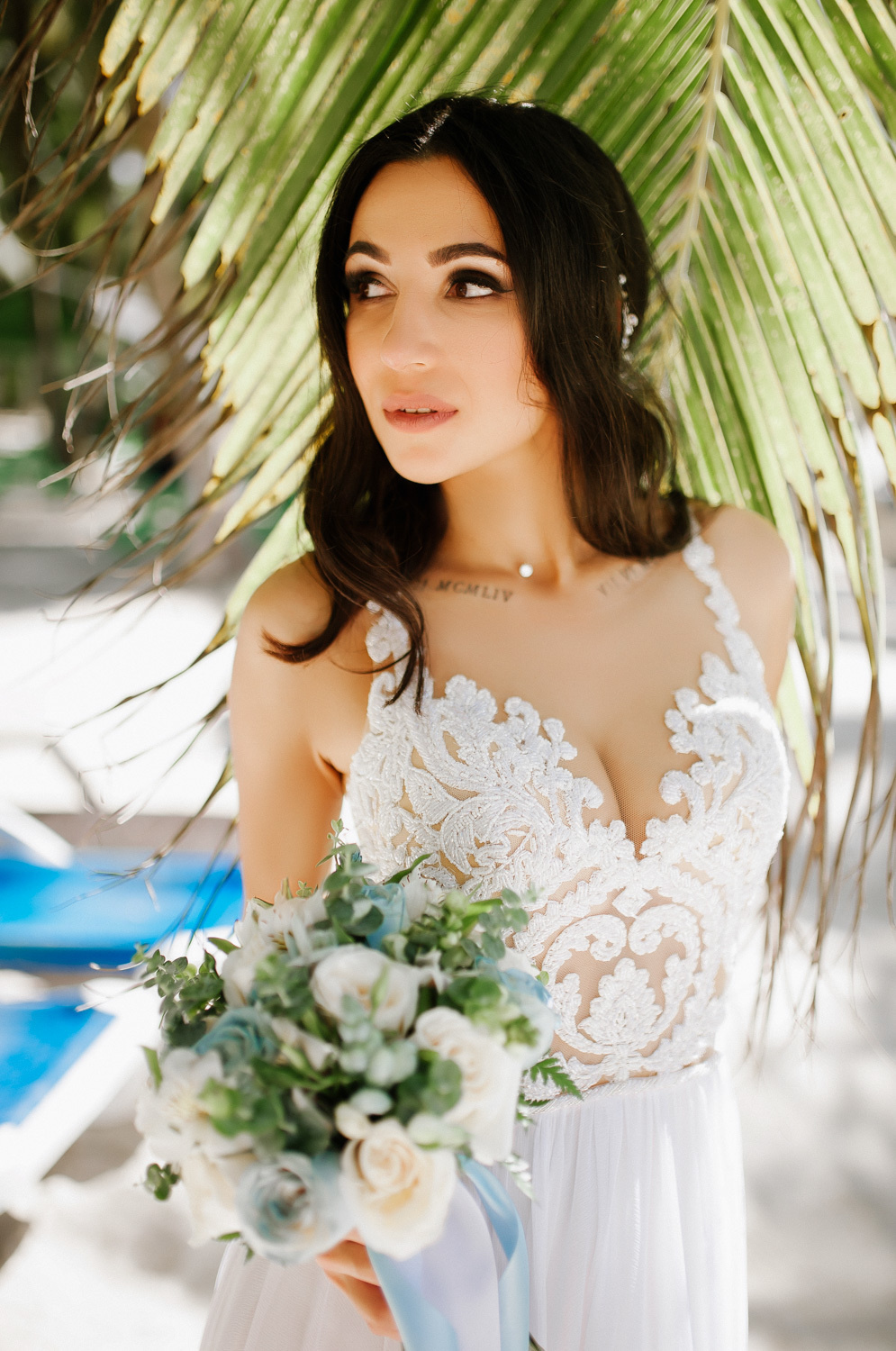 Bride in a wedding dress with a bouquet of flowers on the background of palm leaves.
