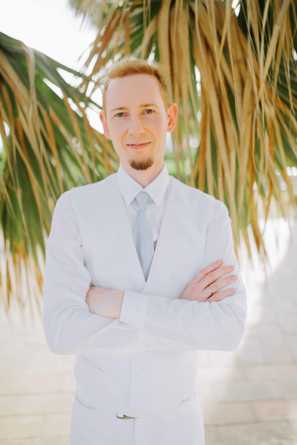 Жених в белой одежде на фоне пальм.