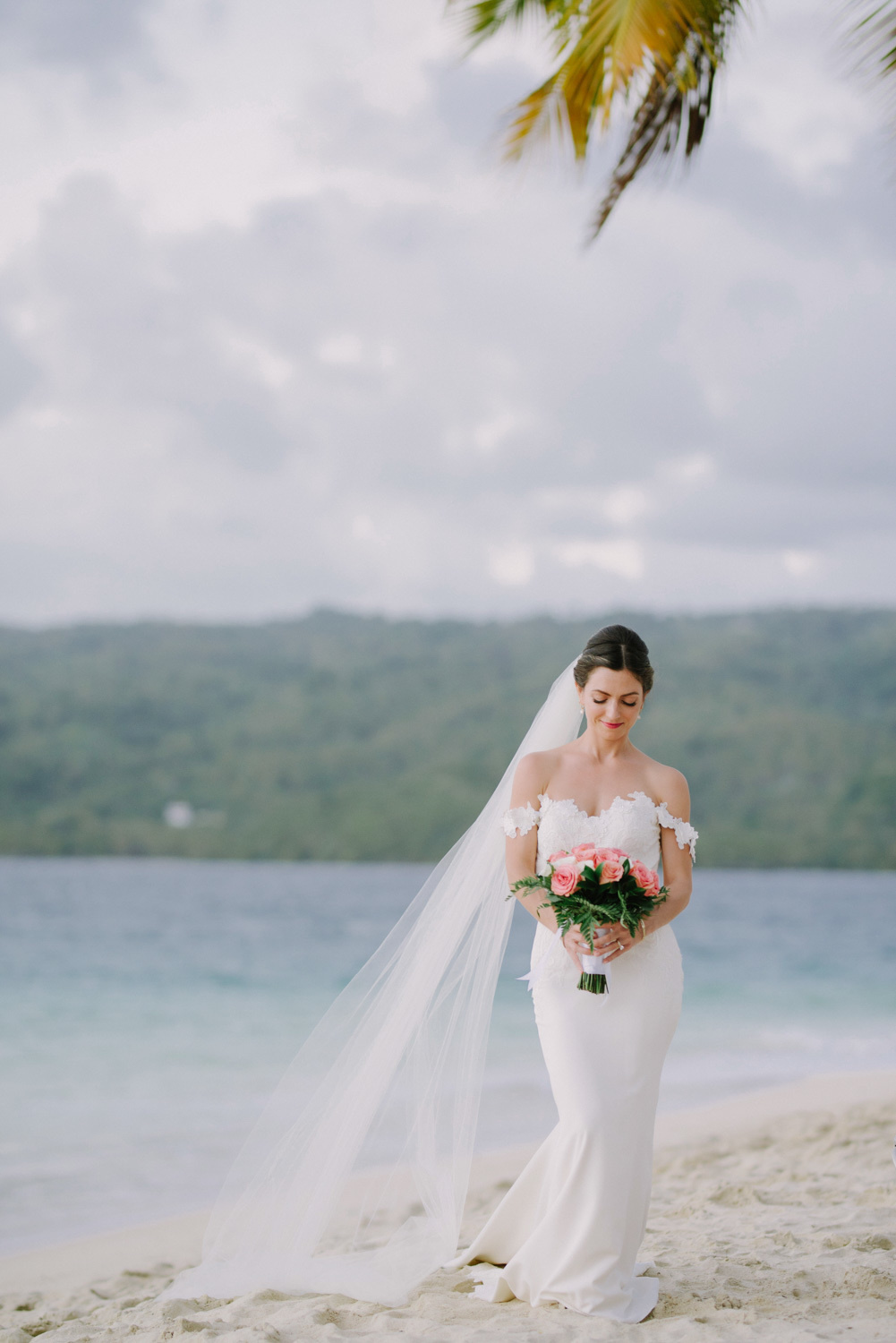 Bride with a bouquet of flowers with a fluttering veil on the background of the sea and the island.