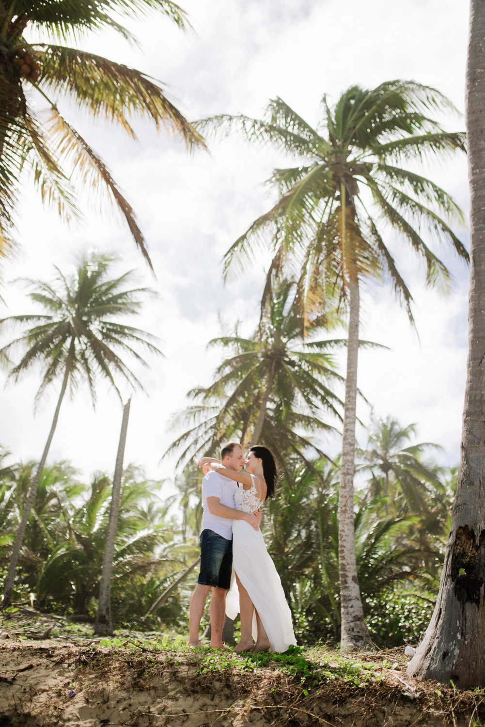 The bride and groom are standing among green palm trees.