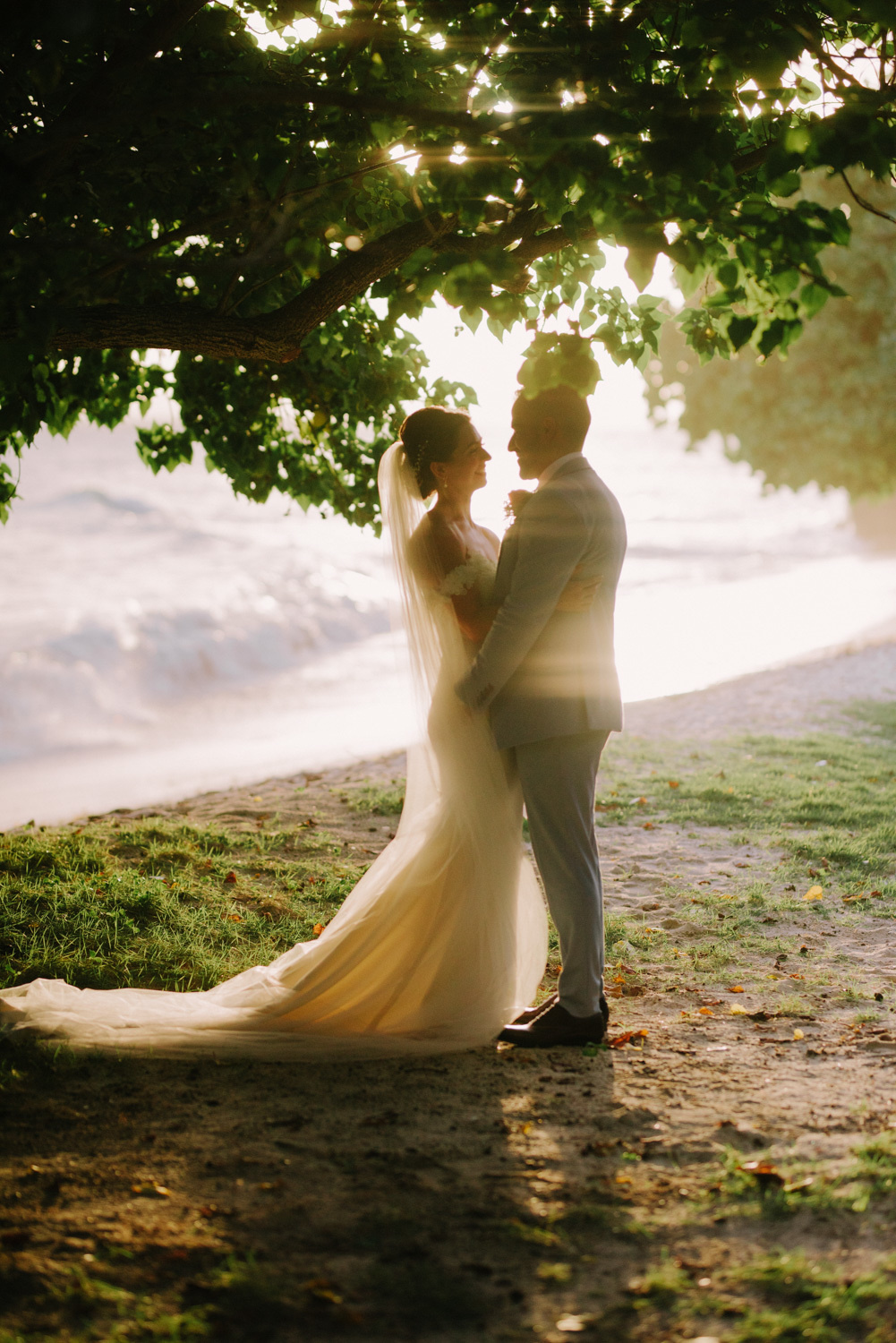 The bride and groom stand in the sunlight.