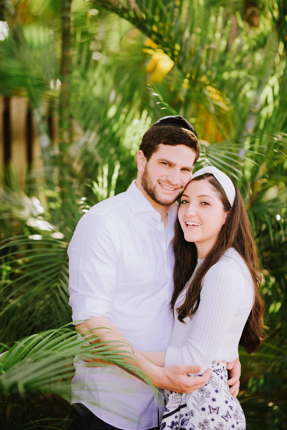 The groom embraces the bride against the background of palm trees.