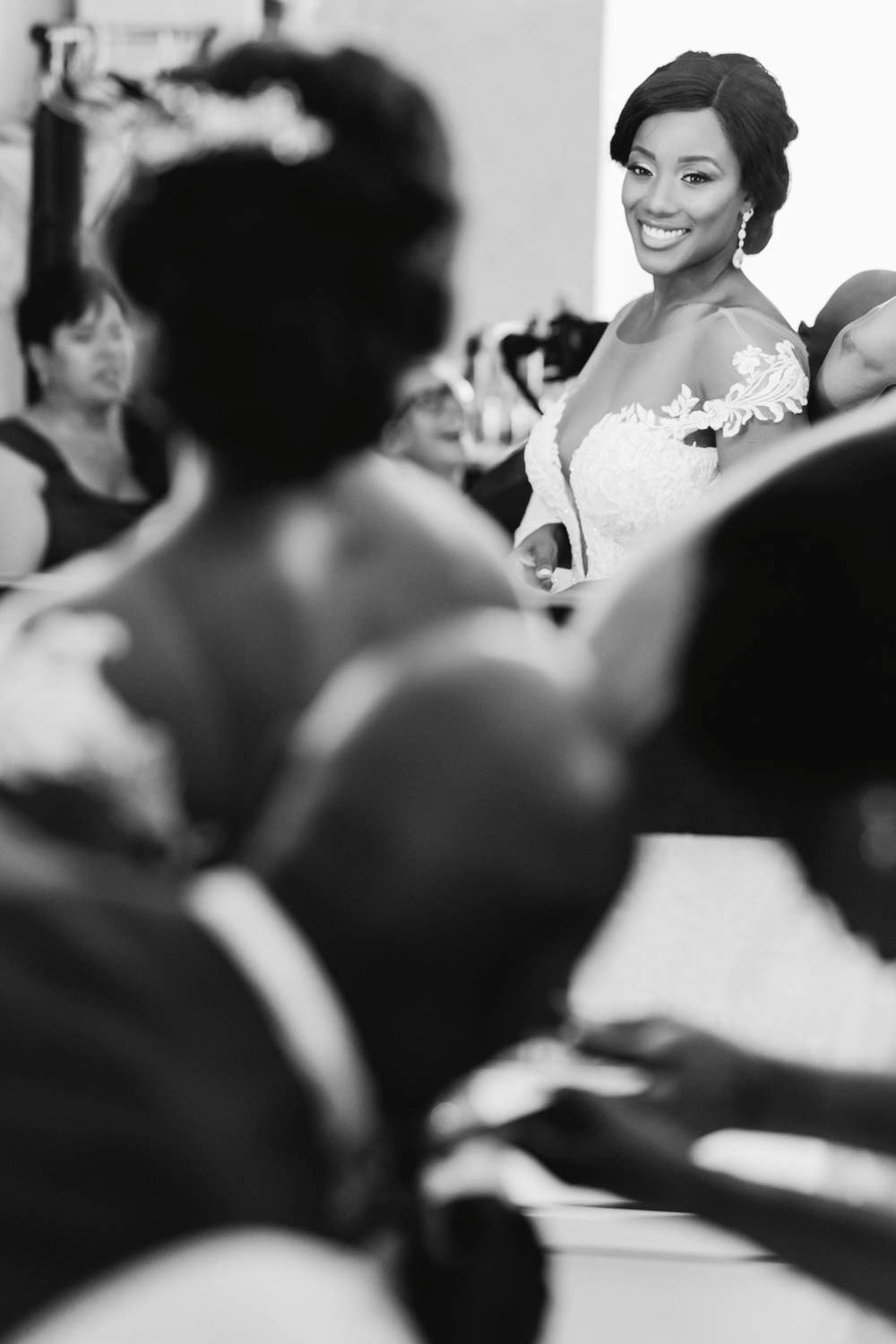 A bride in a wedding dress with a hairstyle and earrings looks at herself in the mirror.