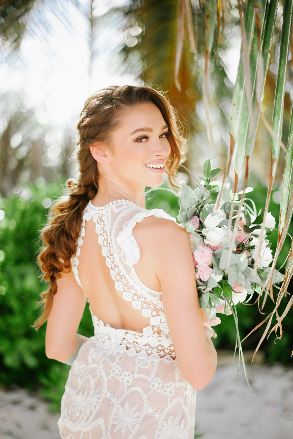 The bride in an open-back openwork white dress with a bouquet of flowers in her hands turned her head back.