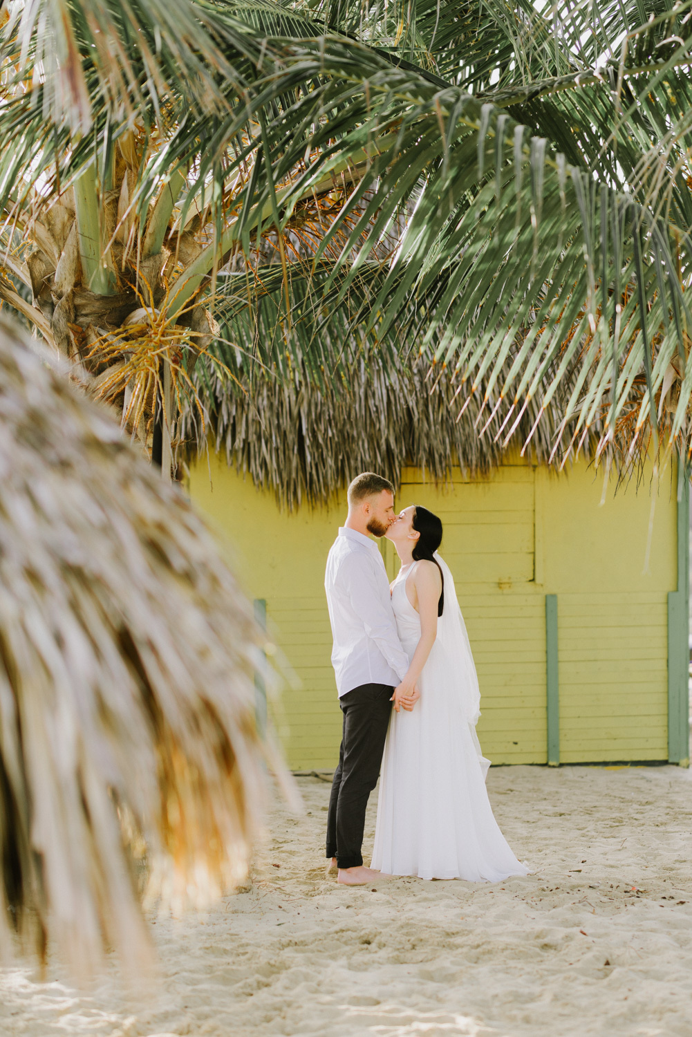 Bride and groom at the beach house under a palm tree.