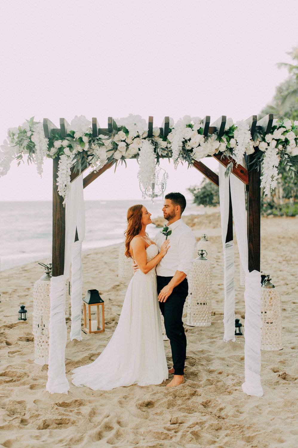 The bride and groom stand at the wedding altar decorated with white bunches of flowers.