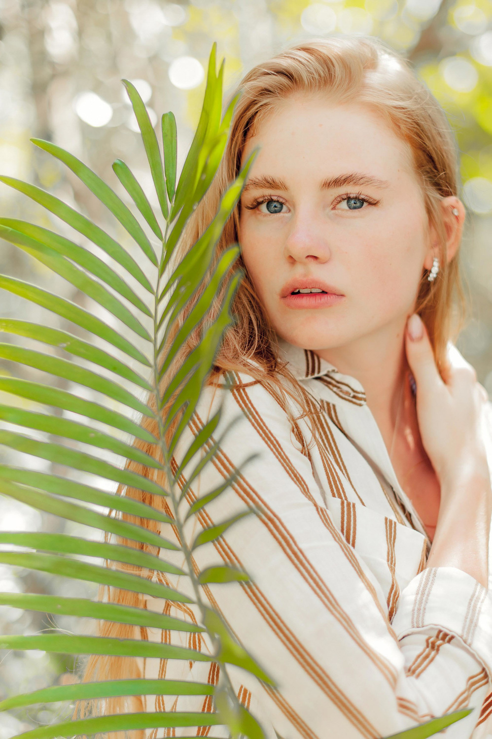 The face of a red-haired girl on the background of a palm leaf.
