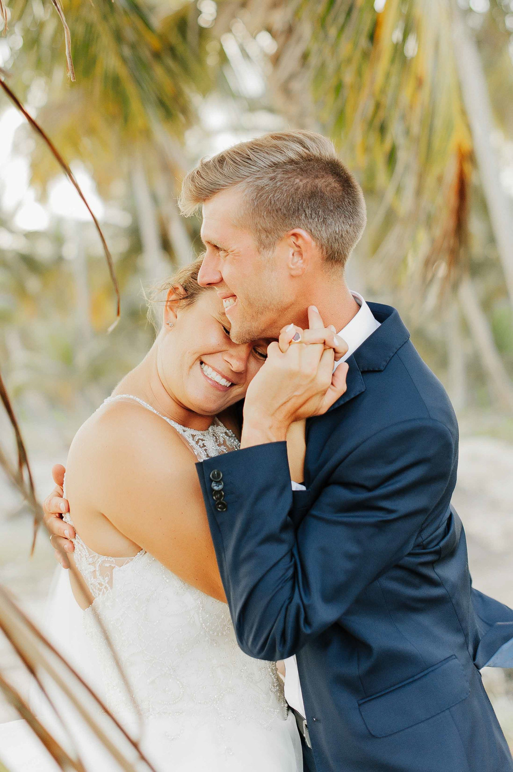 The bride and groom embrace each other on the background of palm trees.