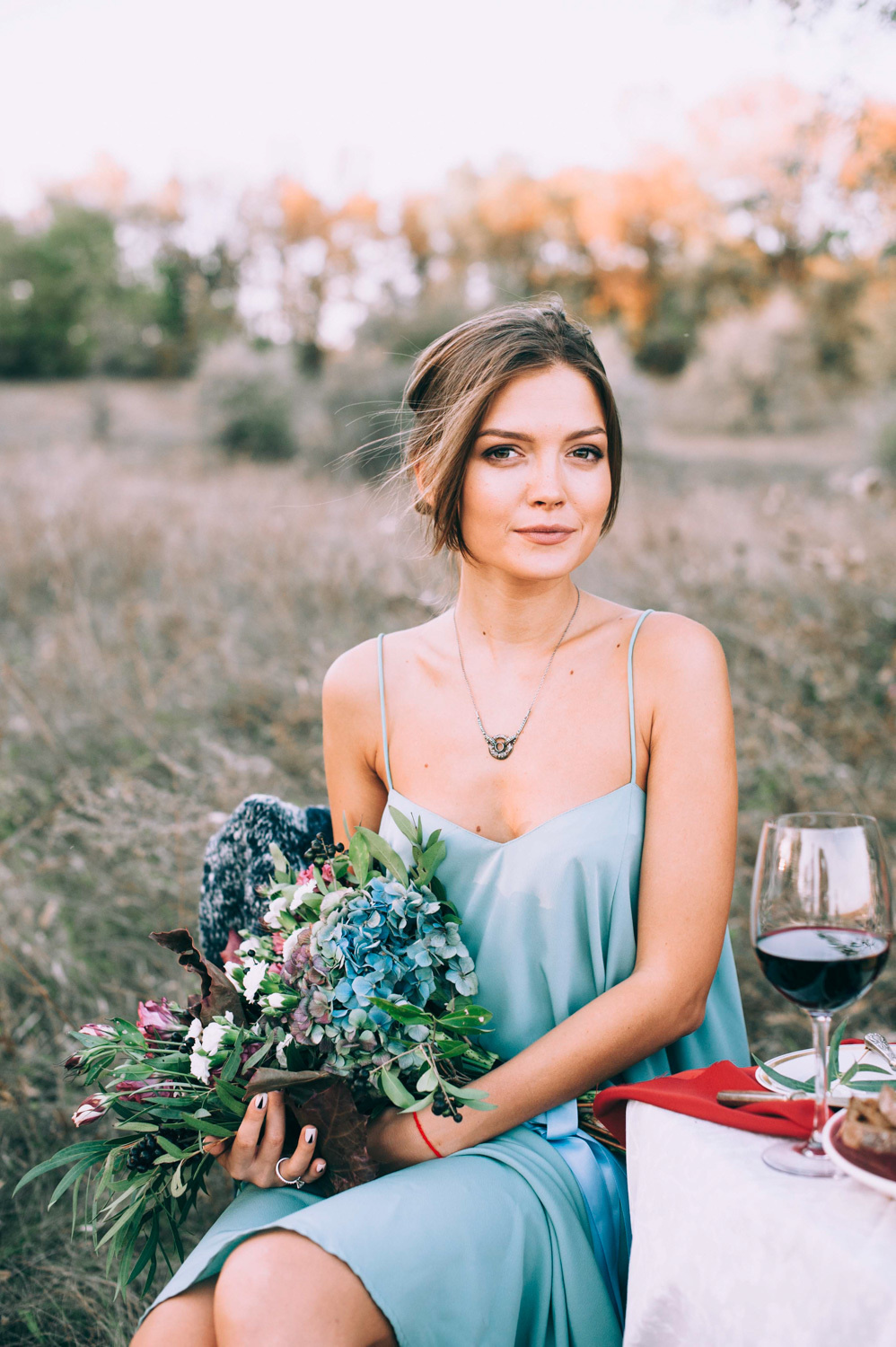 Bride with a bouquet of flowers at the table with a glass of red wine.
