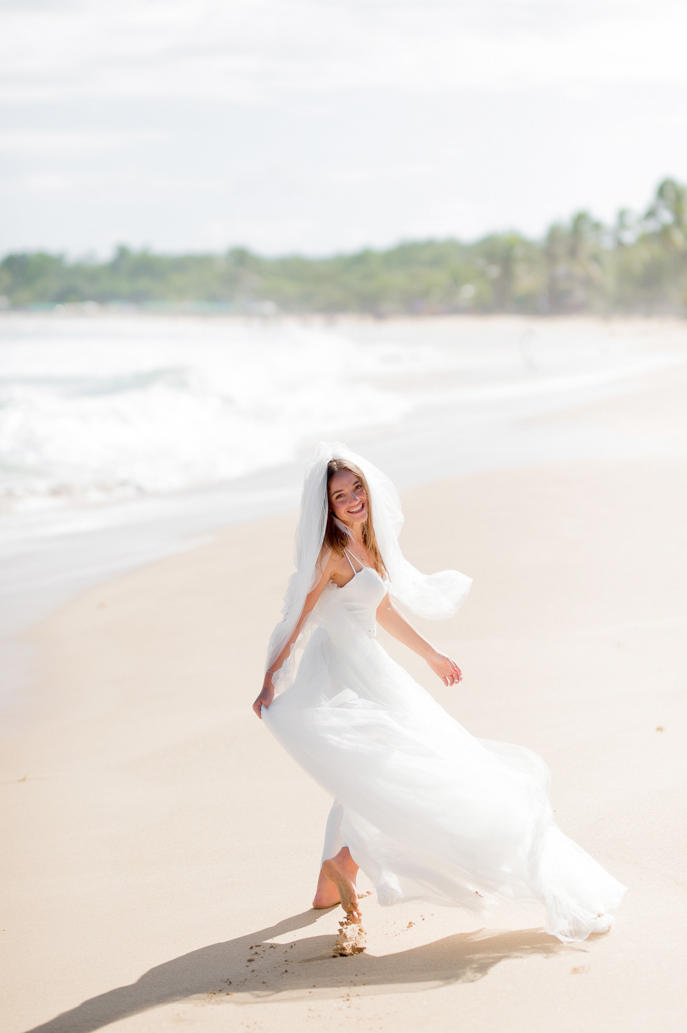 Bride in a dress fluttering in the wind on the background of the sea and the shore with palm trees.